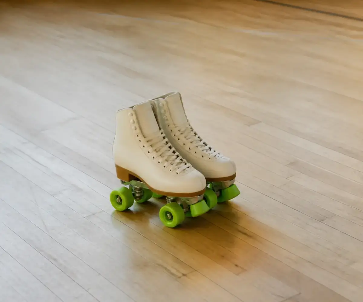 Paire de patins à roulettes quad crème aux roues vert fluo posée sur un parquet clair de piste, vue de trois quarts, lumière douce