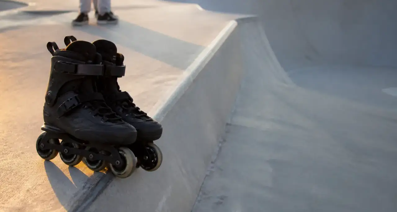 Patins en ligne aux petites roues posés au bord d’une rampe de skatepark en béton, sans inscription, lumière de fin de journée