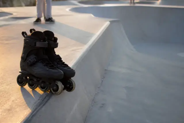 Patins en ligne aux petites roues posés au bord d’une rampe de skatepark en béton, sans inscription, lumière de fin de journée