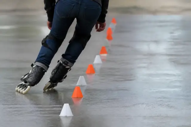 Patineur penché dans un virage serré entre des plots alignés sur un sol lisse, patins en ligne et protections aux genoux, lumière claire