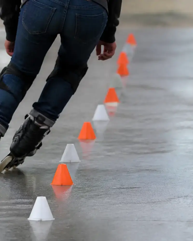 Patineur penché dans un virage serré entre des plots alignés sur un sol lisse, patins en ligne et protections aux genoux, lumière claire