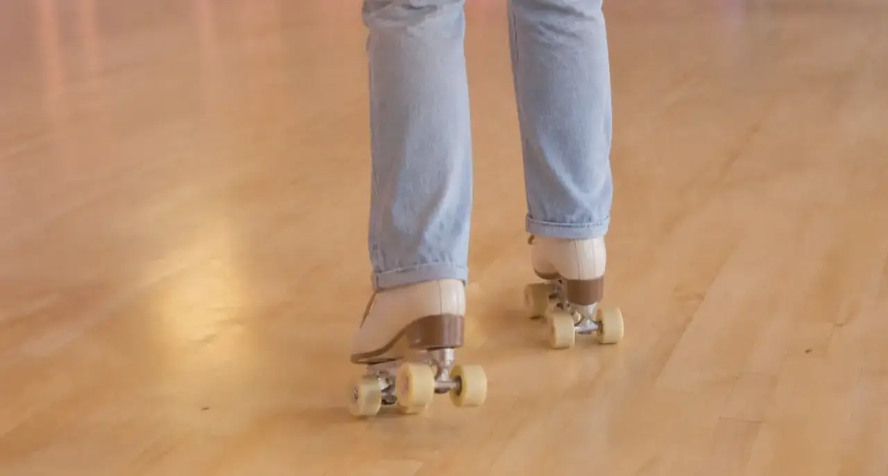 Adulte vu de dos, cadré des genoux aux pieds, chaussé de patins à roulettes quad crème, qui fait ses premiers pas sur un parquet clair