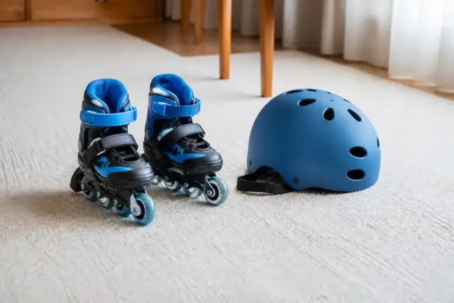 Petits patins à roulettes posés sur un tapis de sol clair, avec un casque pour enfant à côté, sans visage
