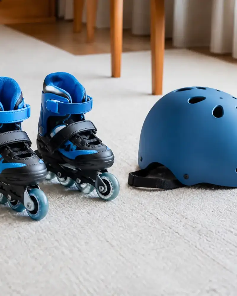 Petits patins à roulettes posés sur un tapis de sol clair, avec un casque pour enfant à côté, sans visage