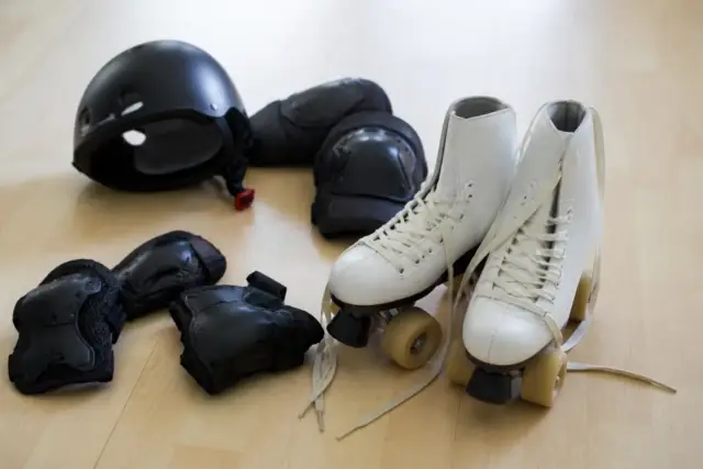 Paire de patins à roulettes posée sur un parquet clair, lacets ouverts, avec un casque et des protections rangés à côté