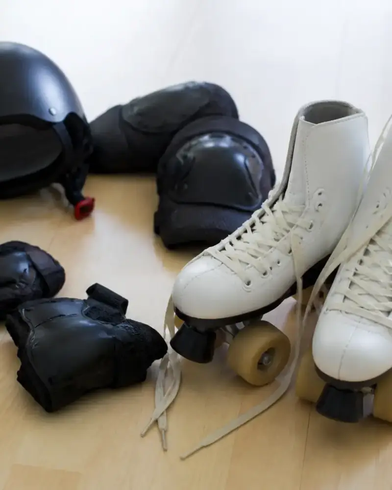 Paire de patins à roulettes posée sur un parquet clair, lacets ouverts, avec un casque et des protections rangés à côté