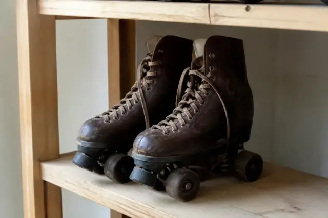 Paire de patins à roulettes quad anciens en cuir patiné posés sur une étagère en bois clair, sans marque ni inscription, lumière douce