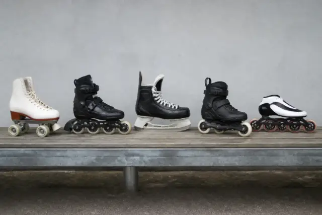 Rangée de cinq patins de types différents posés sur un banc : quad classique, patin en ligne, botte de hockey, patin de freestyle et patin de vitesse