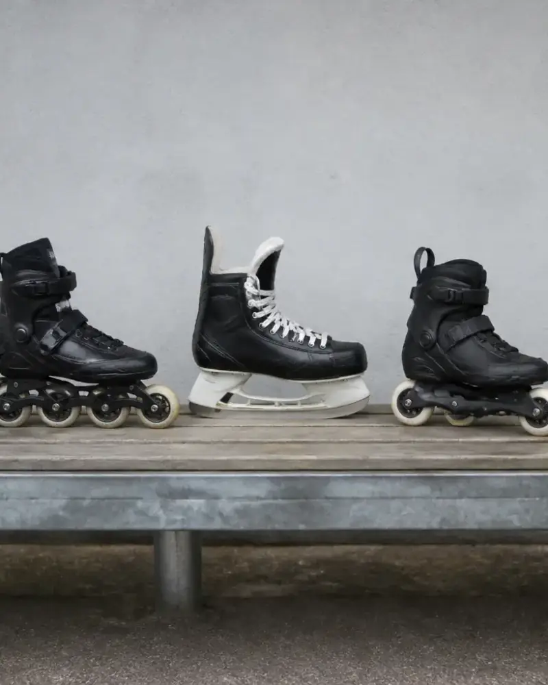 Rangée de cinq patins de types différents posés sur un banc : quad classique, patin en ligne, botte de hockey, patin de freestyle et patin de vitesse