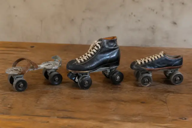 Trois patins à roulettes anciens alignés sur une table en bois, du plus simple aux roues en ligne jusqu’au patin à deux paires de roues