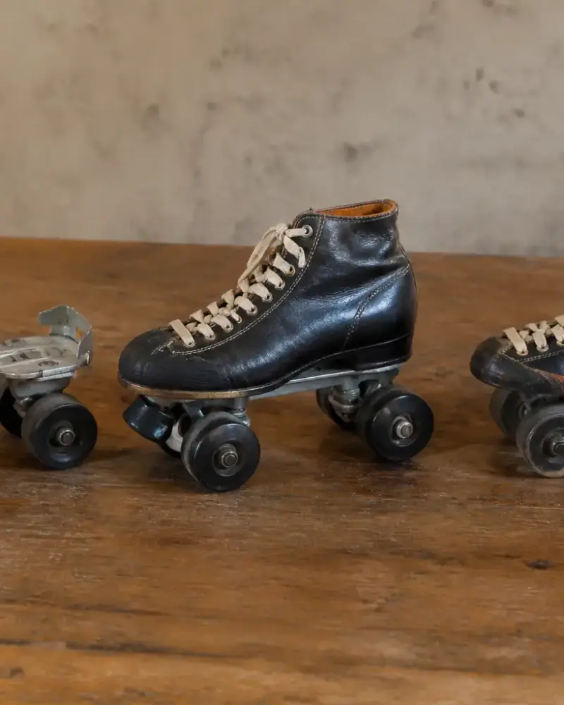 Trois patins à roulettes anciens alignés sur une table en bois, du plus simple aux roues en ligne jusqu’au patin à deux paires de roues