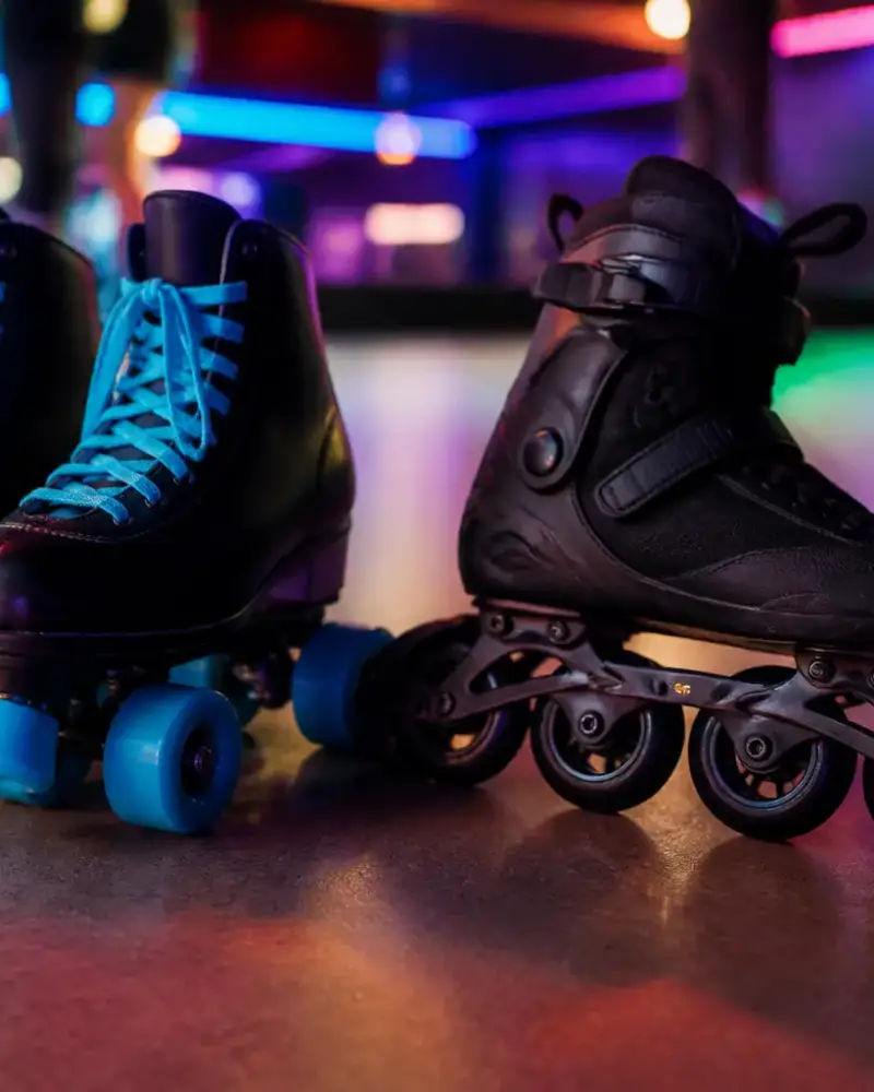 Patins à roulettes à quatre roues vifs posés sur un sol de salle à côté d’un patin à roues alignées, lumière néon douce