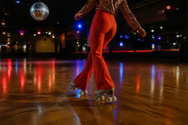 Patineur en tenue colorée des années 1970 dansant sur un parquet ciré sous une boule à facettes, patins à quatre roues aux roues claires