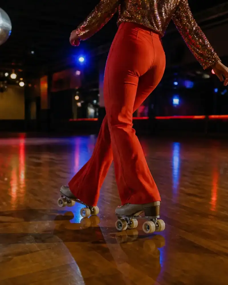 Patineur en tenue colorée des années 1970 dansant sur un parquet ciré sous une boule à facettes, patins à quatre roues aux roues claires