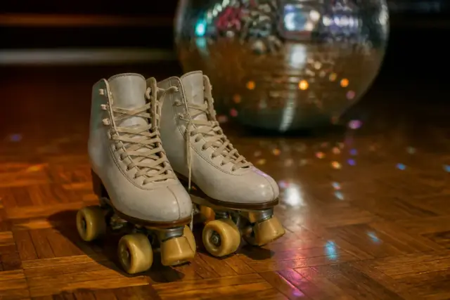 Paire de patins à roulettes à quatre roues aux lacets clairs posée sur un parquet ciré, reflets colorés d’une boule à facettes en arrière-plan