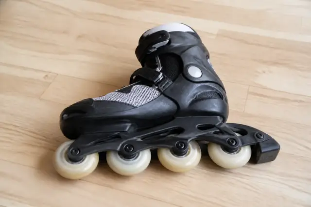 Patin en ligne posé sur le côté sur un parquet clair, roues alignées bien visibles, tampon de frein à l’arrière