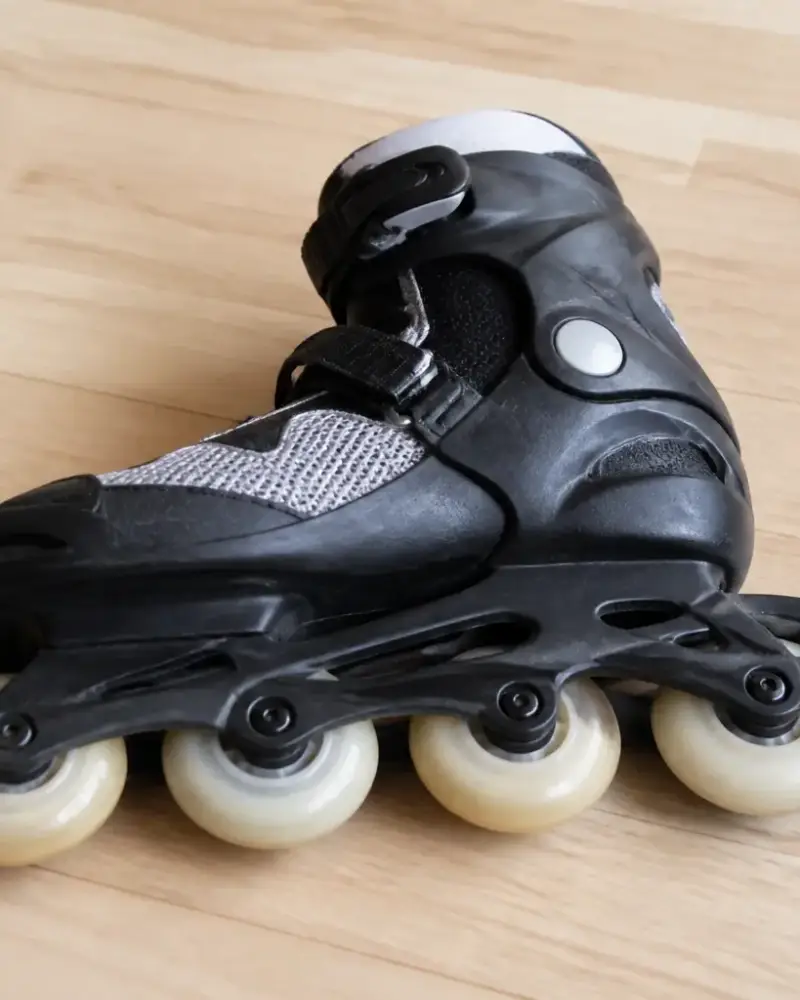 Patin en ligne posé sur le côté sur un parquet clair, roues alignées bien visibles, tampon de frein à l’arrière