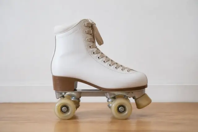Patin à roulettes quad vu de profil sur un parquet clair, botte, platine, deux essieux et quatre roues bien visibles