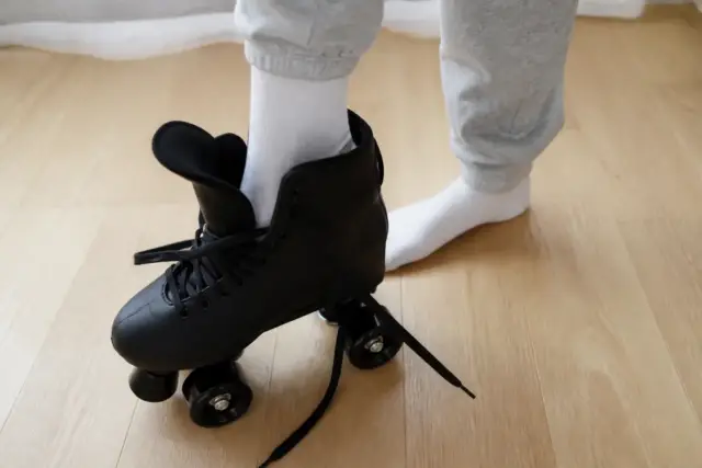 Pied en chaussette posé dans une botte de patin à roulettes ouverte, lacets lâches, parquet clair, sans visage