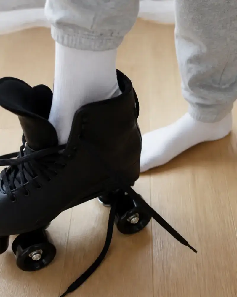 Pied en chaussette posé dans une botte de patin à roulettes ouverte, lacets lâches, parquet clair, sans visage