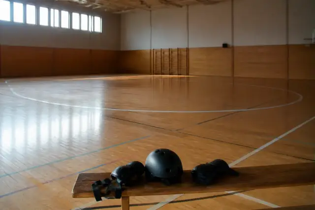 Piste ovale de roller derby vide, lignes tracées au sol d’un gymnase, casque et protections posés sur un banc en bois