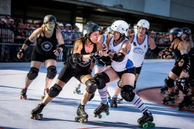 Femmes disputant un match intense de roller derby, casques et protections portées