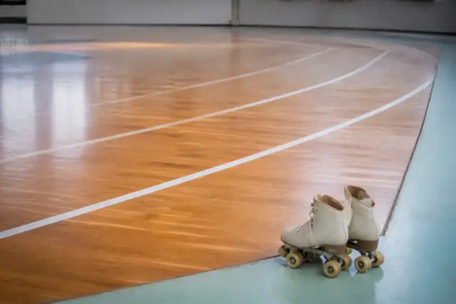 Piste ovale tracée au sol d’un gymnase, lignes claires sur parquet, patins à roulettes quad posés au bord