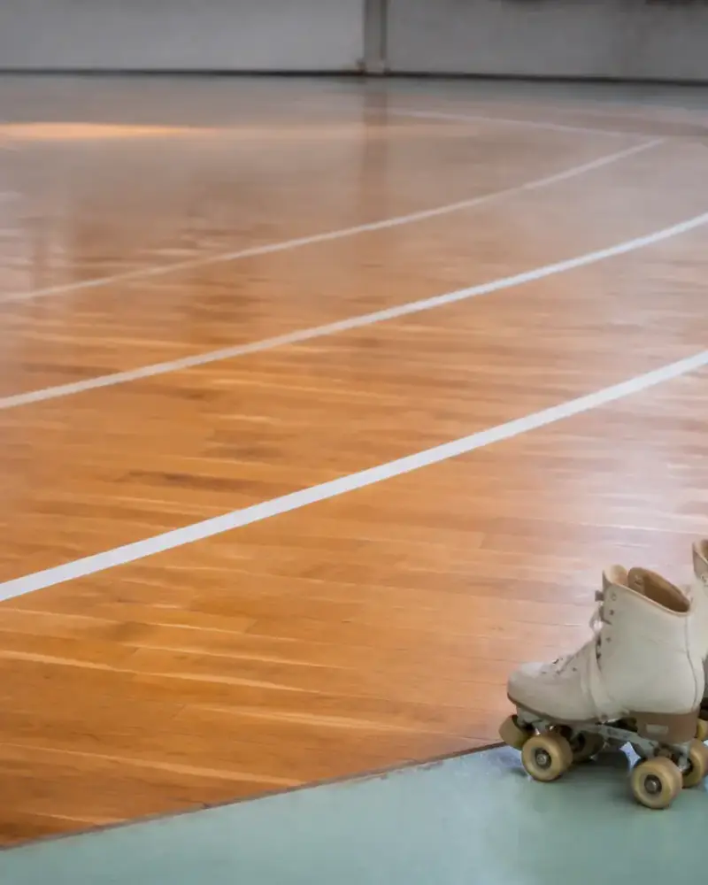 Piste ovale tracée au sol d’un gymnase, lignes claires sur parquet, patins à roulettes quad posés au bord