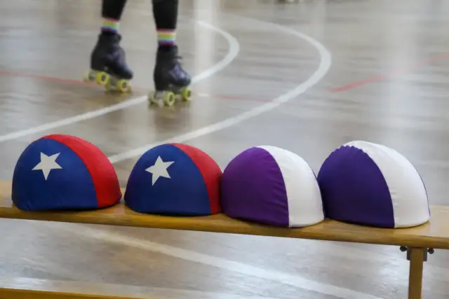 Deux jeux de couvre-casques colorés, l’un avec une étoile, posés sur un banc de gymnase, piste tracée en arrière-plan