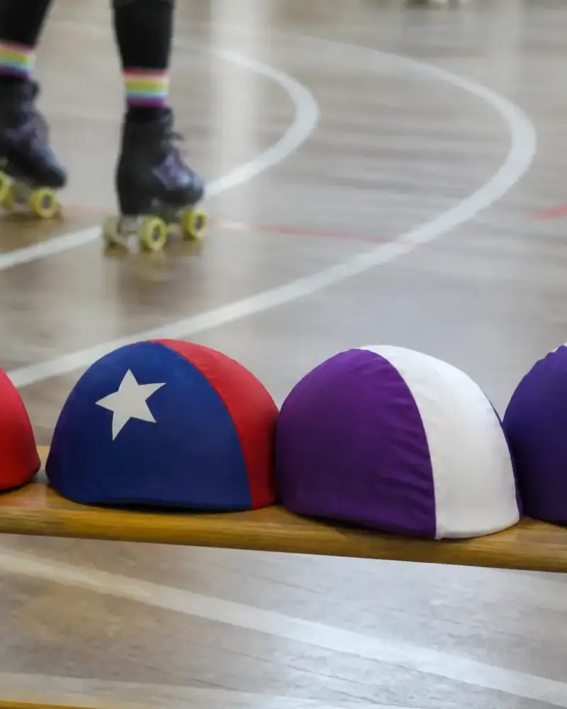 Deux jeux de couvre-casques colorés, l’un avec une étoile, posés sur un banc de gymnase, piste tracée en arrière-plan