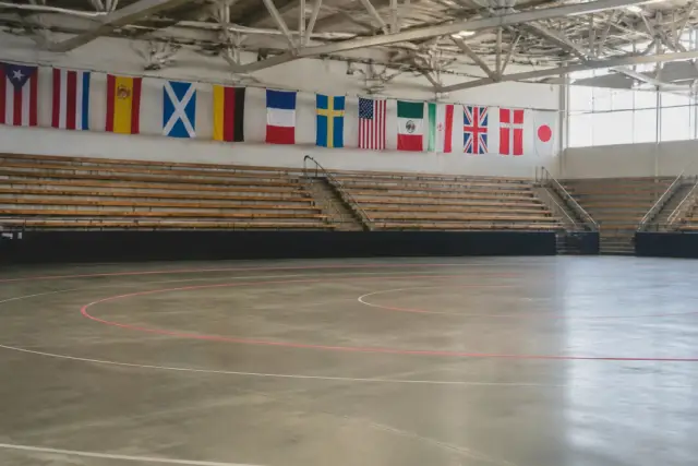 Gradins vides d’une grande salle de sport, piste de roller derby tracée au sol, drapeaux de pays accrochés au mur