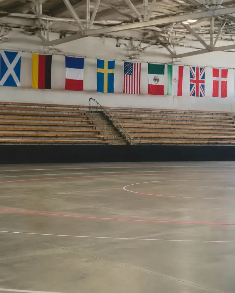 Gradins vides d’une grande salle de sport, piste de roller derby tracée au sol, drapeaux de pays accrochés au mur