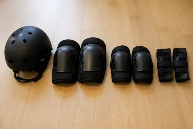 Casque, genouillères, coudières et protège-poignets rangés côte à côte sur un parquet clair, sans marque ni inscription, lumière douce