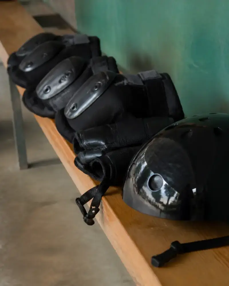 Casque rigide de roller derby sans marque posé sur un banc de bois clair, jugulaire dénouée, genouillères et protège-poignets à côté